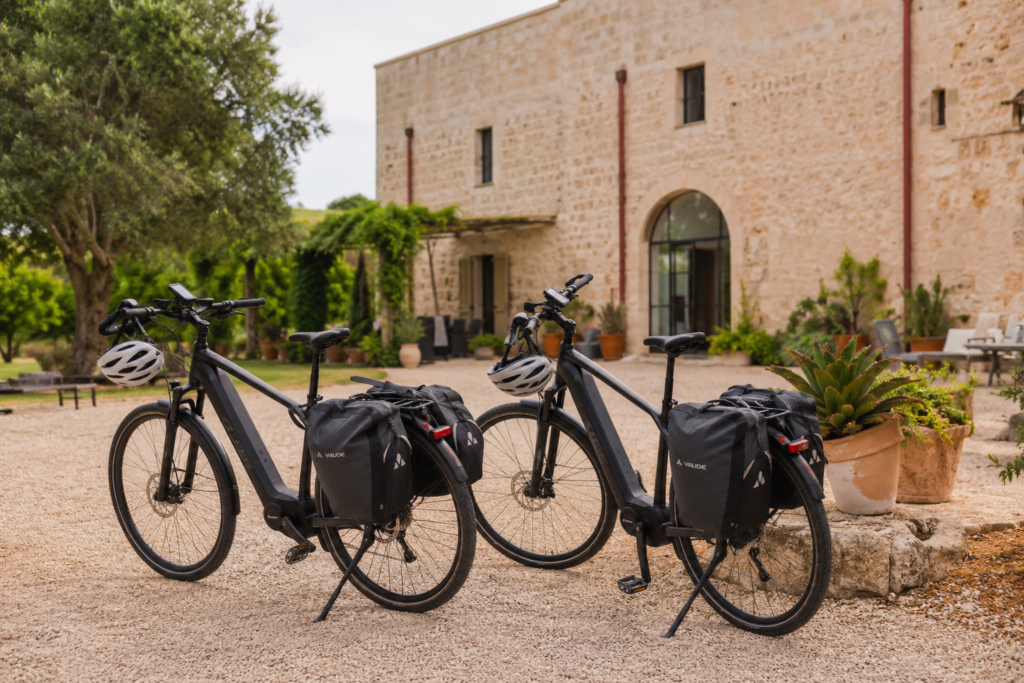 Premium touring e-bikes with bike bags, helmets and GPS navigation prepared outside a traditional countryside masseria in Puglia for self-guided cycling holidays through rural southern Italy