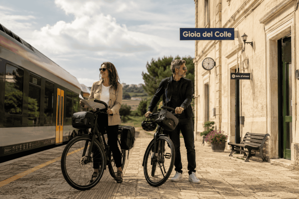 Due persone con ebike alla stazione di Gioia del Colle, Puglia, in attesa del treno.